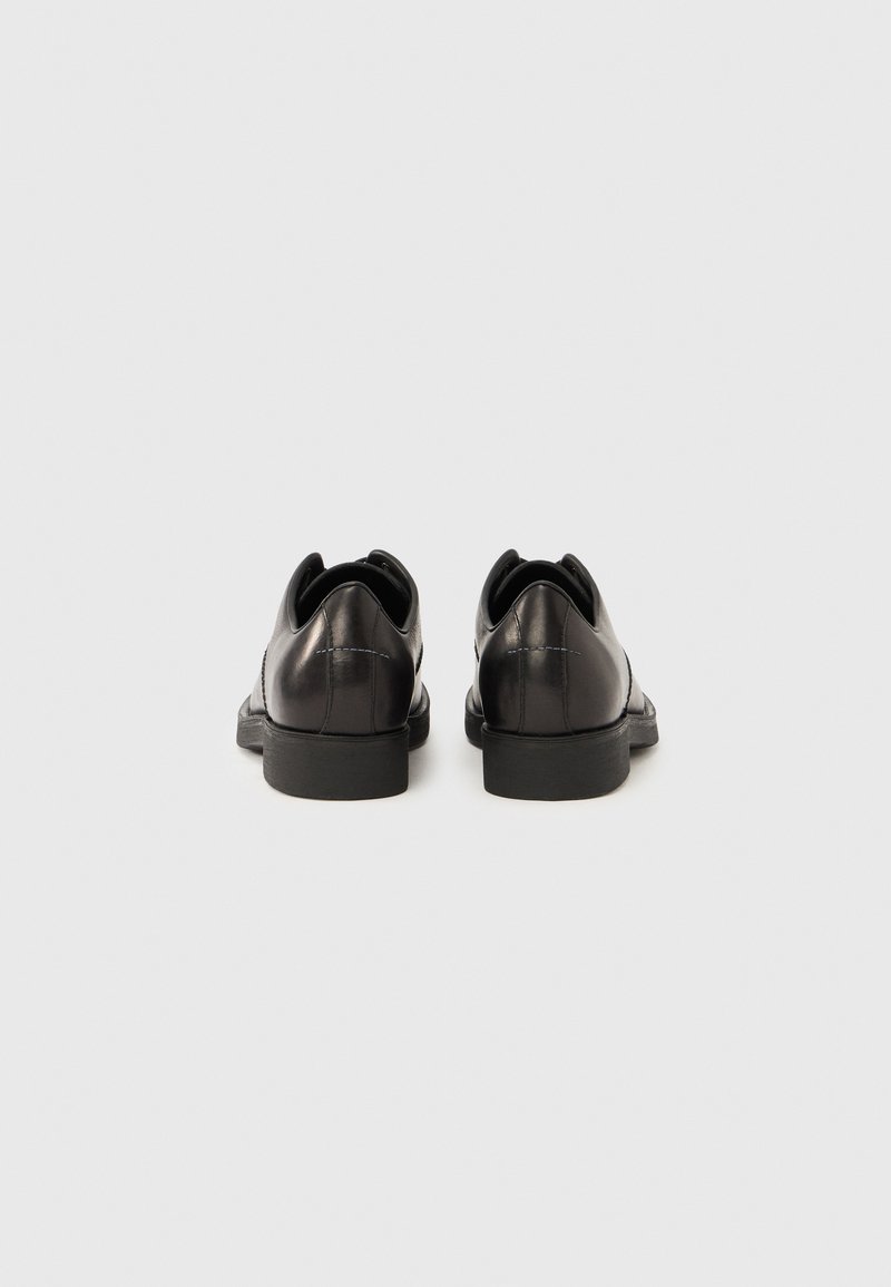 Chaussures en cuir noir à finition lisse, bout arrondi et petit talon. Design minimaliste avec un détail de couture discret à l'arrière.