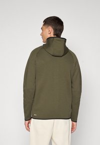 Sweat à capuche vert olive avec une capuche ajustée, des manches raglan et des accents noirs aux poignets et à l'ourlet. Tissu lisse, peu de marquage.