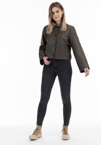 Kürzerer dunkelgrüner Lederjacke mit Knopfverschluss, weiten Ärmeln, kombiniert mit schwarzen engen Jeans und hellbraunen Schnürstiefeletten.