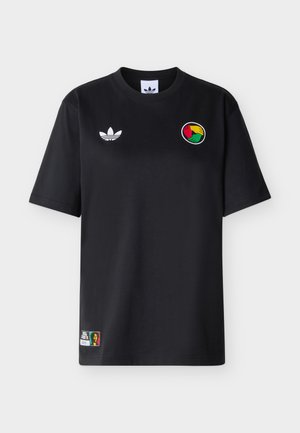 Camiseta negra de manga corta con logo blanco de Adidas, emblema circular de mano en rojo, amarillo y verde en el pecho, y pequeño parche multicolor cerca del dobladillo.