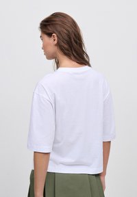 T-shirt bianco a maniche corte in cotone con una vestibilità rilassata. Presenta un colletto a giro e un orlo dritto, abbinato a una gonna verde.