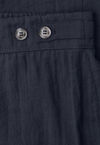 Dark blue fabric with two round, light-colored buttons sewn on a waistband with stitched details.