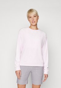 Ανοιχτό ροζ φούτερ με σχέδιο διαμαντιών, στρογγυλή λαιμόκοψη και ριμπ μανίκια· σε συνδυασμό με σορτς με σχέδιο σε αποχρώσεις ναυτικού και λευκού.