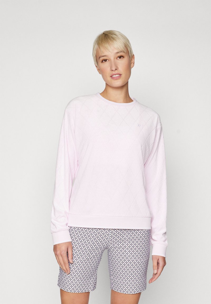 Ανοιχτό ροζ φούτερ με σχέδιο διαμαντιών, στρογγυλή λαιμόκοψη και ριμπ μανίκια· σε συνδυασμό με σορτς με σχέδιο σε αποχρώσεις ναυτικού και λευκού.