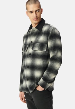 Camicia in flanella a quadri bianca e nera con colletto, due tasche sul petto e bottoni neri. Materiale strutturato con una finitura pattern.