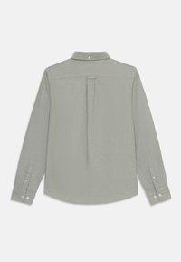 Camisa de manga larga de tela verde claro, con un pliegue en la parte posterior, cuello con botones y puños abotonados con acentos de botón único.