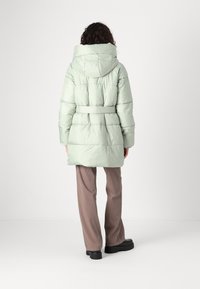 Puffjakke i lys mintgrønn, med belted midje, stor hette og elastiske mansjetter. Glatt, glansfull tekstur med quiltet design.
