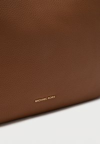Καφέ δερμάτινη τσάντα με υφή, με χρυσό λογότυπο "MICHAEL KORS" στην κάτω δεξιά γωνία.