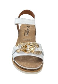 Witte sandaal met een gouden kettingaccent, verstelbare enkelband en een gestructureerde binnenzool. Gemaakt in Spanje, met een platte hak en subtiele stiksels.