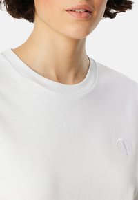 Weißes Baumwoll-T-Shirt mit geripptem Rundhalsausschnitt, das ein dezentes gesticktes Logo auf der Brust, eine glatte Textur und einen lässigen Schnitt bietet.
