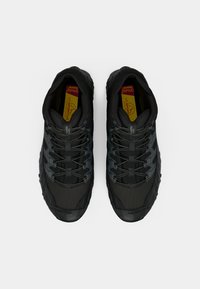 Sapatos esportivos pretos com parte superior em malha texturizada, detalhes cinzentos e atacadores elásticos. Apresentam uma palmilha com amortecimento e uma sola robusta.