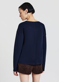 Maglione oversize blu navy con scollo rotondo, maniche lunghe, finitura testurizzata e una cucitura centrale distinta, abbinato a pantaloncini di velluto a coste marroni.