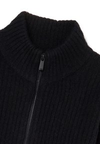 Pull en maille côtelée noir avec un col montant et une fermeture éclair sur le devant. Le tissu semble doux et texturé, avec un design épuré et minimal.