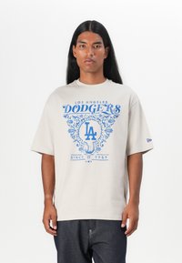 Beige bomulds t-shirt med et blåt Los Angeles Dodgers logo og dekorative elementer, afslappet pasform og korte ærmer.