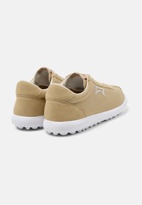 Tan suede sneakers with white soles, featuring lace-up design, back pull tab, and subtle branding on the heel and side.