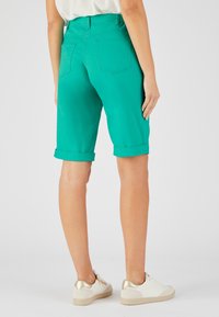 Bermudas turquesas con dobladillo enrollado y bolsillos traseros, hechas de una tela suave. El modelo las combinó con zapatillas blancas con detalles en dorado.