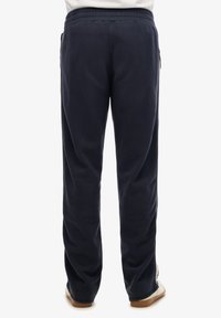 Pantalones de chándal azul marino con cinturilla elástica, bolsillos laterales y un corte relajado. Textura suave con un acabado liso y diseño de perneras ajustadas.