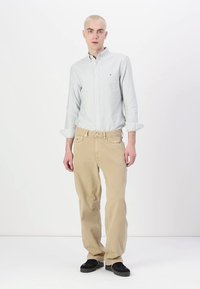 Lichtblauw en wit gestreepte overhemd met knopen, beige broek en zwarte schoenen. Het overhemd heeft lange mouwen en de broek heeft een rechte pijp.