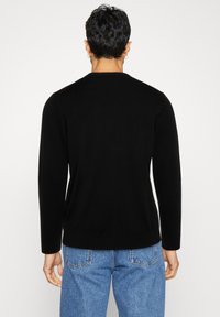 Čierny sveter s dlhým rukávom z pletenej látky, s okrúhlym výstrihom, priliehavým strihom a rebrovanými manžetami, nosený s svetlomodrými rifľami.