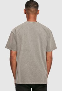 Camiseta gris de manga corta con cuello redondo clásico, fabricada en un tejido suave y con detalles de costura visibles en las mangas y el dobladillo.