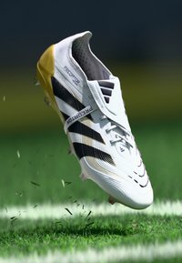 White soccer cleat with purple and black accents, textured surface, low profile, and visible laces. It appears to be floating above grass.