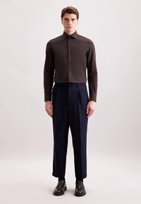 Bruin overhemd met knoopsluiting en lange mouwen, gedragen met marineblauwe broek; zwarte schoenen; gladde textuur; slank model.