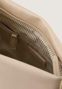 Beige Lederhandtasche mit einem Reißverschlussfach im Inneren, ausgestattet mit einem gestreiften, beige-weißen Futter. Glatte Textur, minimalistisches Design.