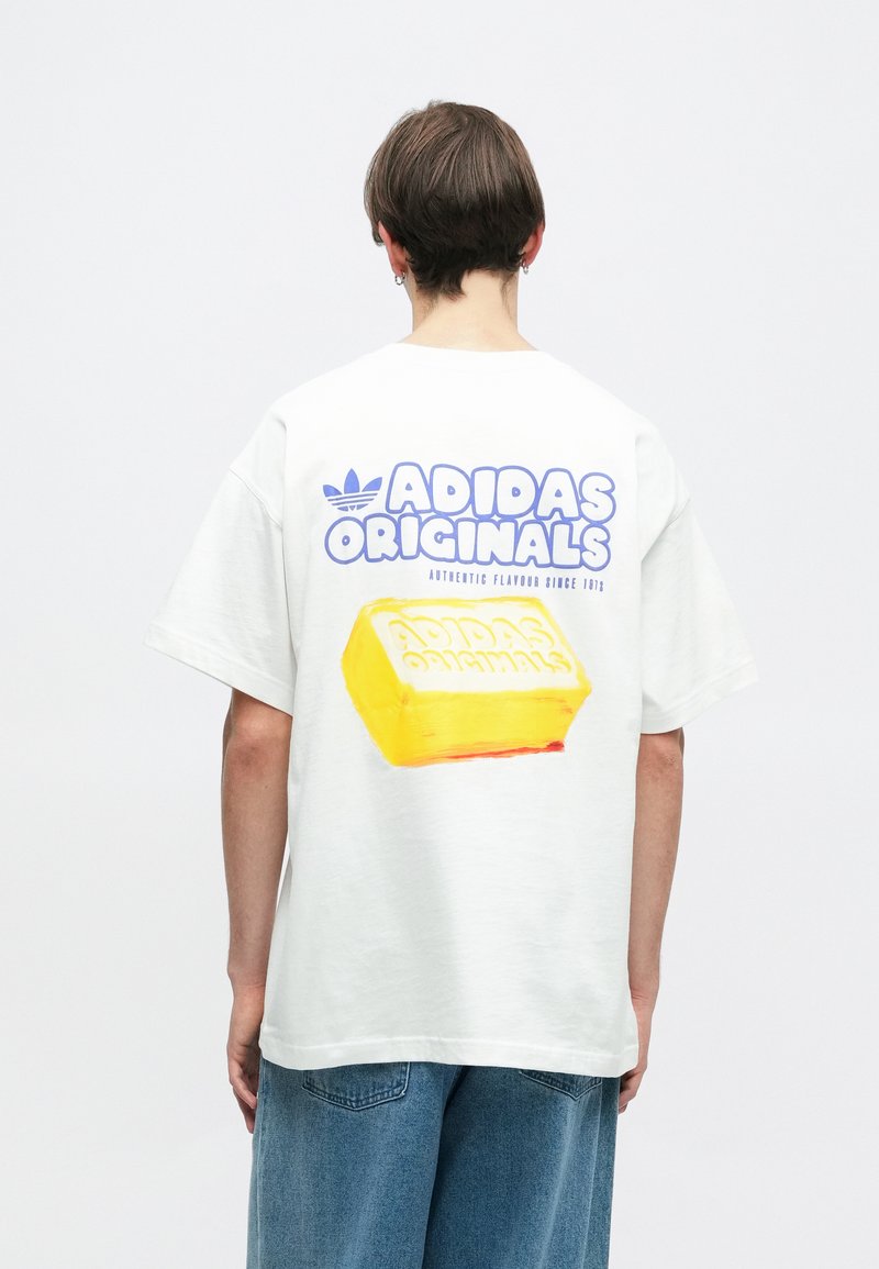 Witte katoenen t-shirt met een grote gele blokgrafiek op de achterkant met "ADIDAS ORIGINALS" in blauwe tekst. Korte mouwen en een relaxte pasvorm.