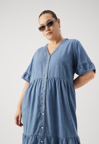 Blå chambray-kjole med v-hals, korte volangermper, knappestolpe og rynket, tiered skjørt. Glatt tekstur og uformell design.