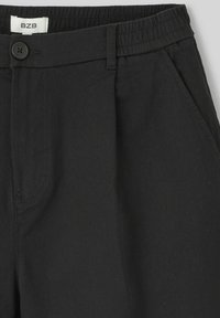 Pantalons noirs en tissu doux avec une texture lisse, dotés d'une fermeture à bouton, d'une taille élastique et de poches latérales inclinées.
