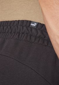 Svarta sportshorts med en ribbad midjeband och en liten Puma-logg. Närbild som visar textur och sömdetaljer.