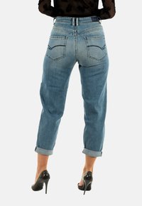 Jeans de mezclilla azul claro con un corte relajado, dobladillos doblados y dos bolsillos traseros con parches que presentan detalles de costura sutiles.