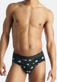 Schwarze Slips mit weißen dreieckigen Mustern, elastischem Bund und glatter Stoffoberfläche. Sie verfügen über ein eng anliegendes Design und minimalen Sitz.