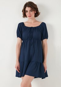 Navy blue dress with a square neckline, short puff sleeves, and a cinched waist. Features a tiered skirt and a soft, textured fabric.