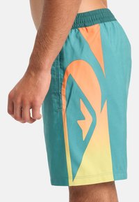 Tyrkysové plavky s oranžovým a žlutým gradientem a velkým logem, s elastickým pasem a boční kapsou.