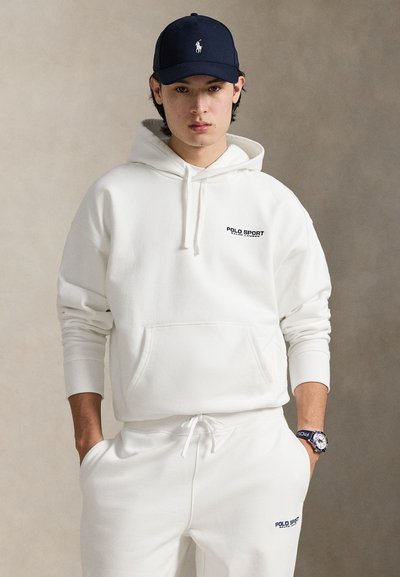 Hvit hettegenser med frontlomme og svart "POLO SPORT"-logo; kombinert med matchende joggebukser og en marineblå caps med logo.