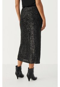 Jupe midi noire en sequins avec une taille serrée et une silhouette droite. Présente une surface texturée et un léger éclat, associée à des bottines noires à la cheville.