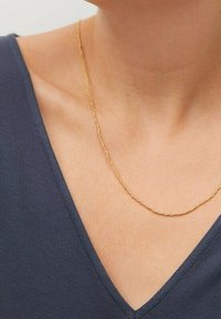 Collana a catena dorata attorcigliata posata su pelle nuda; che completa un top blu navy con scollo a V. Texture liscia con un design elegante e semplice.