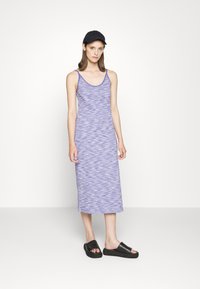 Vestido maxi roxo sem mangas com riscas horizontais, combinado com sandálias pretas de deslizar. Apresenta um decote redondo e uma silhueta justa.
