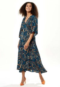 Flowing teal dress with orange and cream marble patterns, featuring a V-neck and loose sleeves, paired with orange high-heeled shoes.