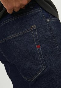 Dunkelblaue Denim-Jeans mit Kontrastnähten, einem roten Akzent auf der Gesäßtasche, strukturiertem Stoff und klassischem Fünf-Taschen-Design.