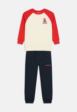 Sweat-shirt crème et rouge à manches longues pour enfant avec un petit motif de skate en dessin animé, associé à un pantalon de survêtement bleu marine avec un texte rouge "Skate Crew".