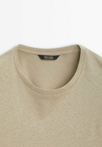 T-shirt beige en lin et coton avec encolure ronde et étiquette noire à l'intérieur du col indiquant la marque et les détails du matériau.