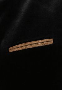 Schwarzer Samtstoff mit einem schmalen Akzentstreifen aus braunem Leder, strukturierten Oberfläche und einem eleganten, minimalistischen Design.