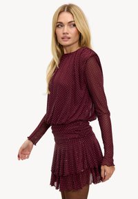 Robe bordeaux à motif à pois, dotée de manches longues transparentes, d'une taille froncée et d'un ourlet à volants superposés. Tissu au toucher doux.