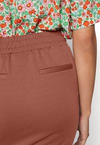 Bruna byxor med elastisk midja, två horisontella bakfickor och en slät textur. Blommönstrad topp med korta ärmar, prydd med rosa och gröna blommor.