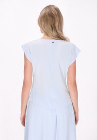 Blusa azzurra chiara con maniche corte a sbuffo, caratterizzata da una sottile cucitura sul retro e un piccolo dettaglio argentato al collo. Tessuto dalla consistenza liscia.