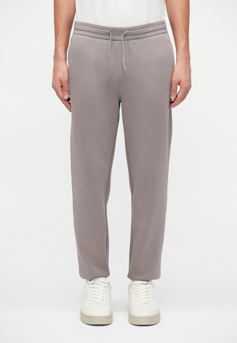 Pantaloni de trening gri, confecționați dintr-un material moale, cu talie elastică și șnur ajustabil, având o croială lejeră și picioare conice.
