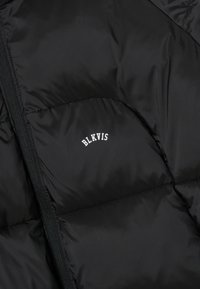 Doudoune noire avec un design matelassé. Dotée d'une fermeture éclair et d'un petit logo blanc "BLKVIS" sur le côté gauche. Texture lisse et brillante.