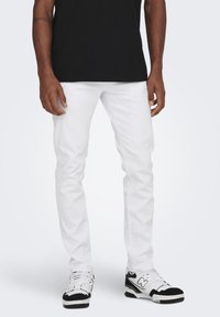 White denim jeans with a slim fit, featuring a classic five-pocket design. Paired with black athletic shoes.
